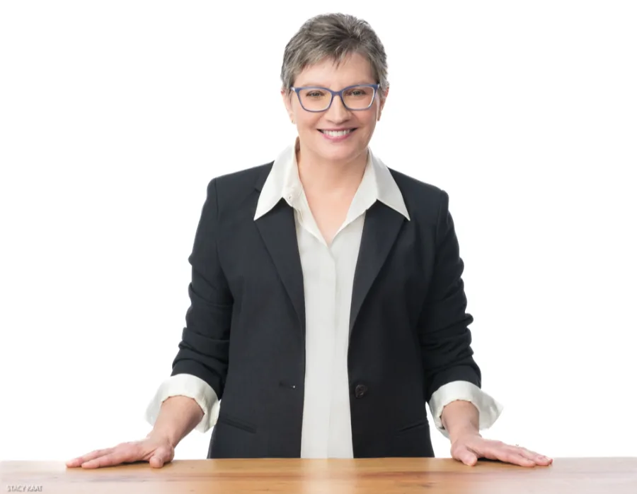 Kathy J. Lang standing with hands flat on desk, smiling and wearing a black blazer